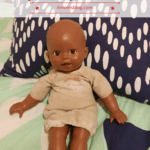 A doll is sitting on the bed with pillows.