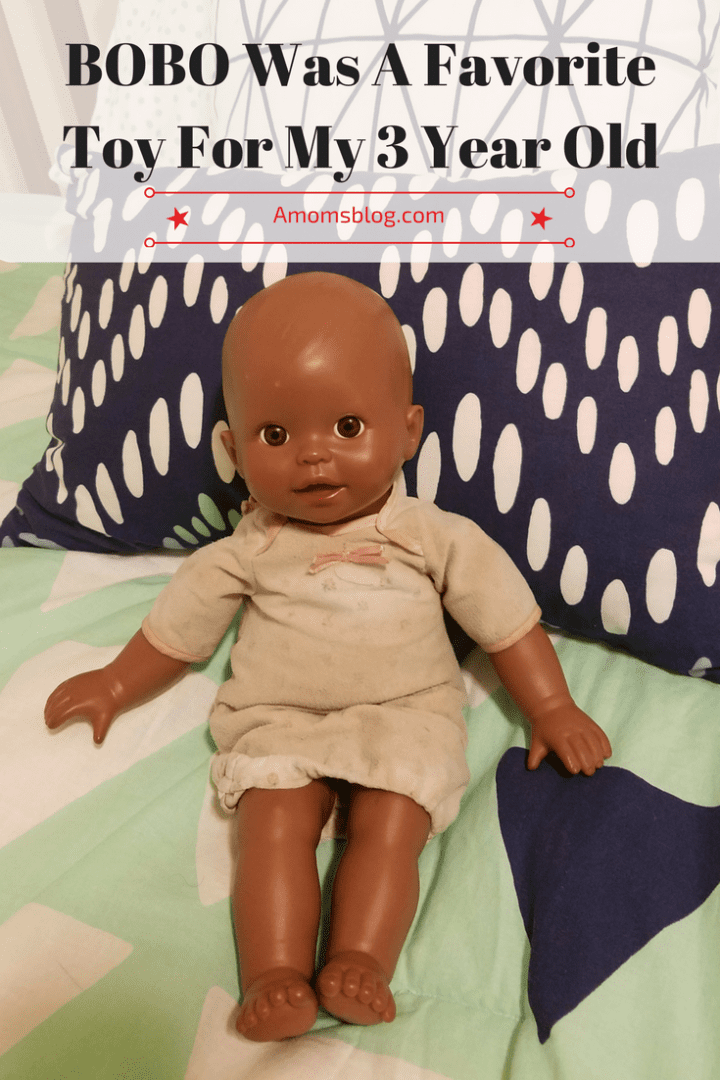A doll is sitting on the bed with pillows.