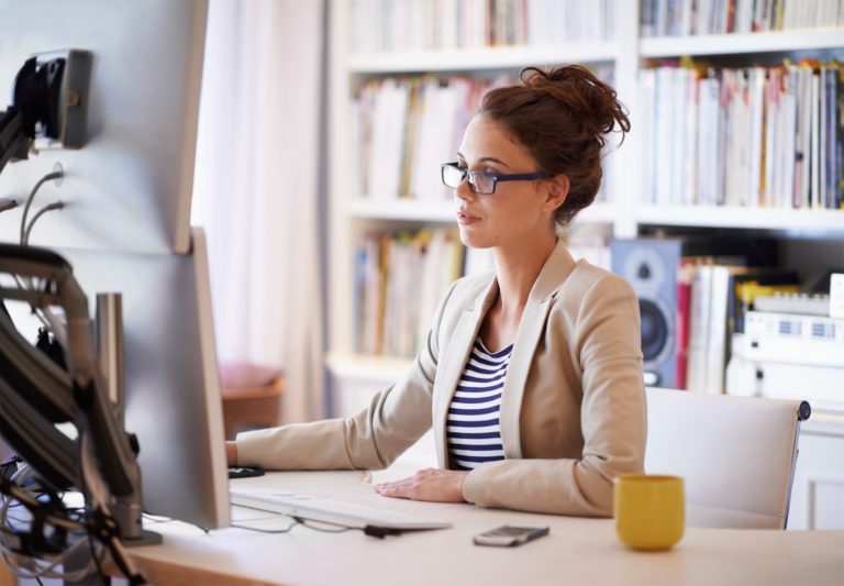 A woman sitting at her desk looking at the computer screen.