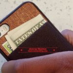 A person holding an iphone case with money sticking out of it.