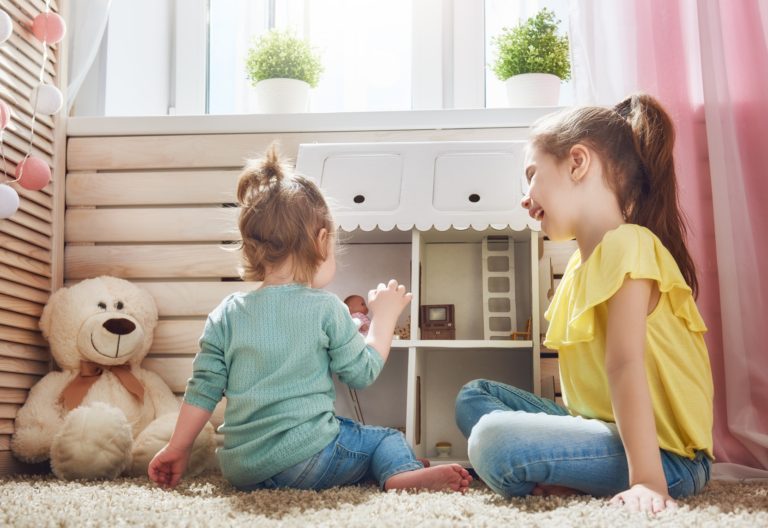 Two little girls sitting on the floor next to a teddy bear.