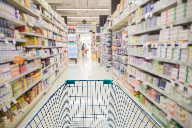 A grocery store aisle with shelves of food and a shopping cart.