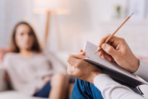 A person writing on paper while sitting in front of another person.