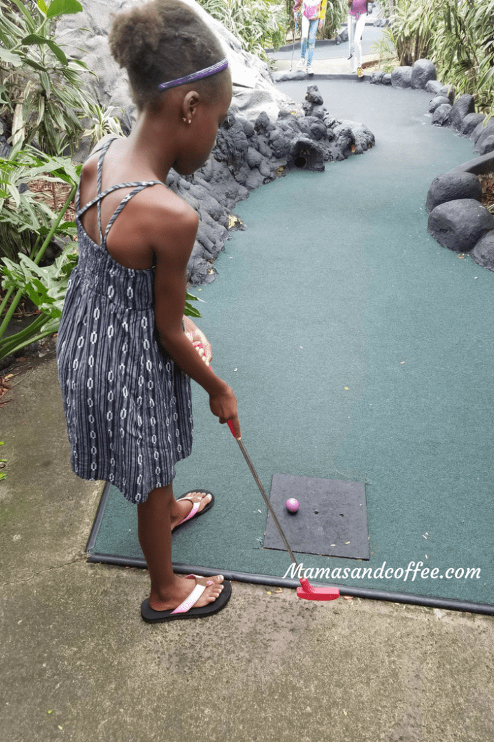 A young girl playing mini golf at the park.