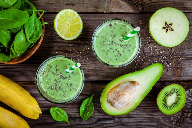 A wooden table topped with two glasses of green smoothie.