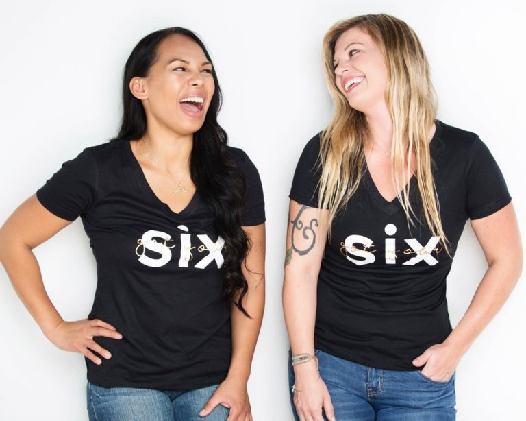 Two women wearing black shirts with the word six on them.
