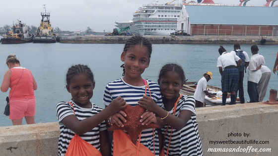 Three girls holding bags in front of a cruise ship.
