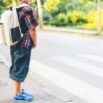 A boy with a backpack standing on the side of the road.