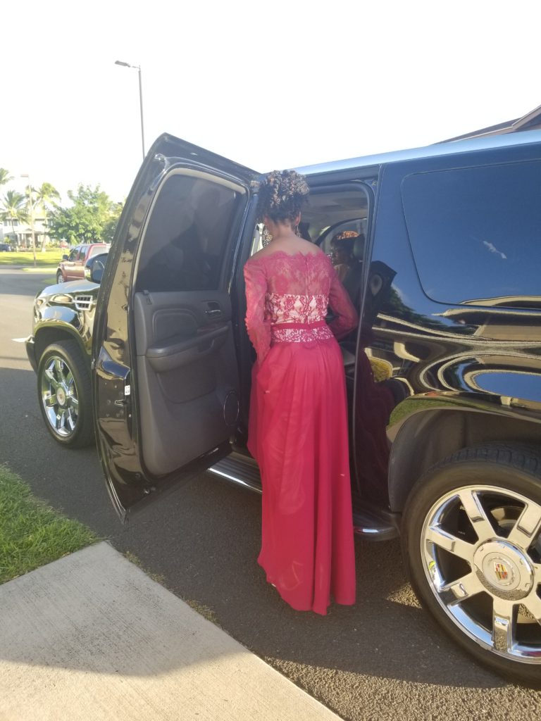 A woman in a long dress standing next to an suv.