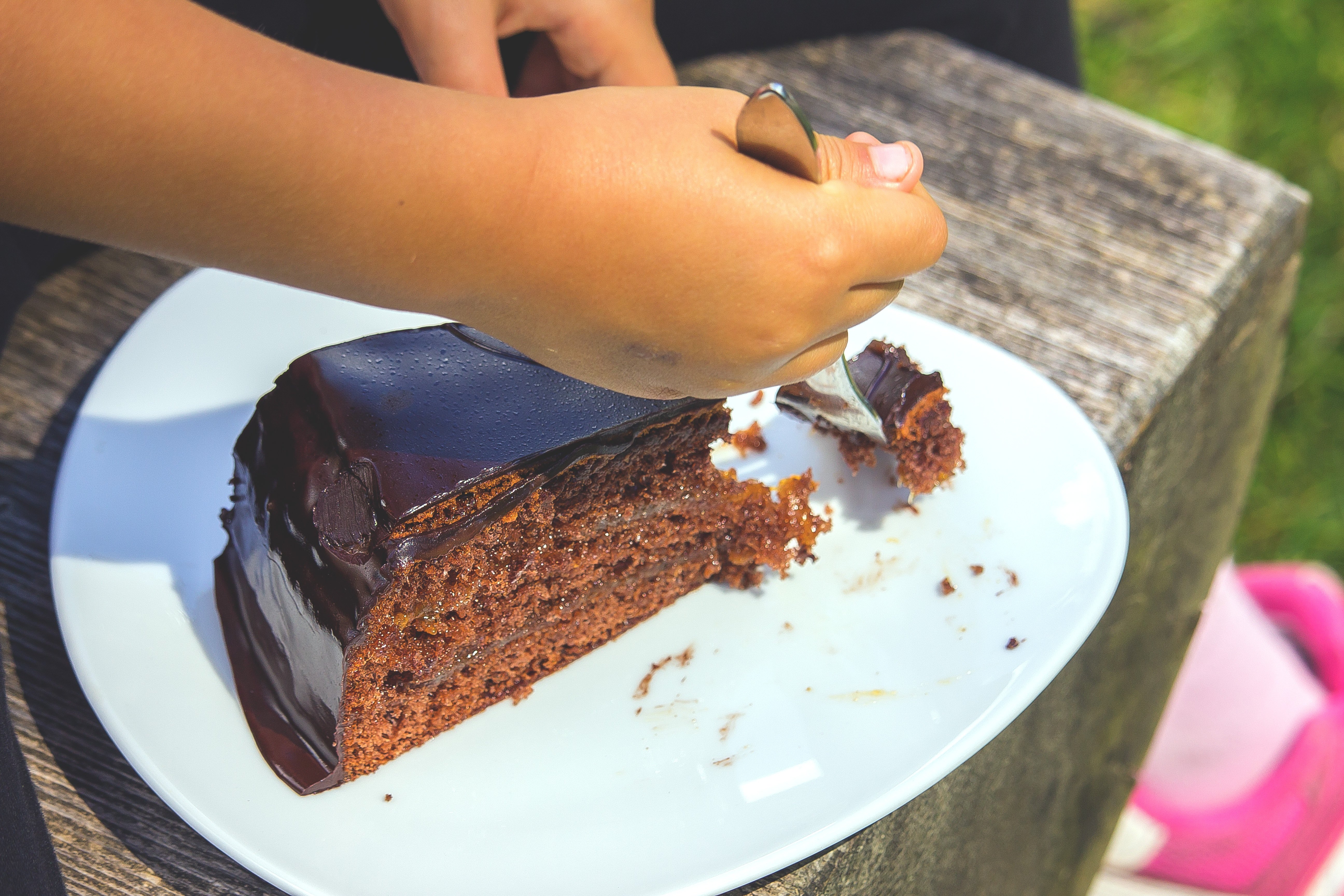 A person cutting into a chocolate cake on top of a white plate.