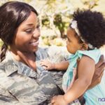 A woman in fatigues holding a child.