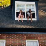 Two girls sitting on a roof of a house.