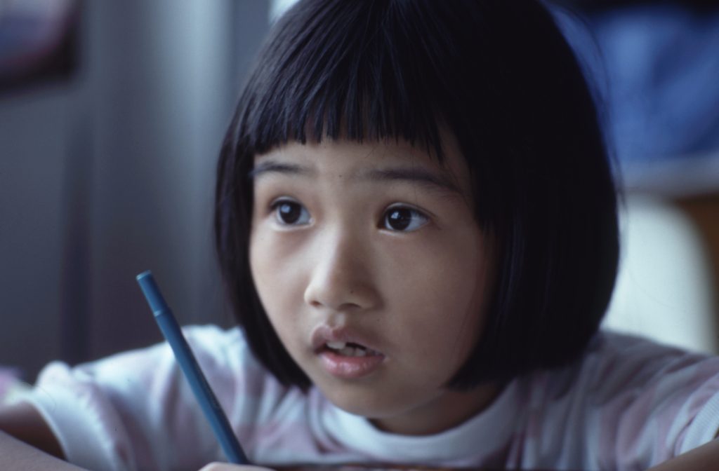 A young girl holding a pencil and looking at the camera.