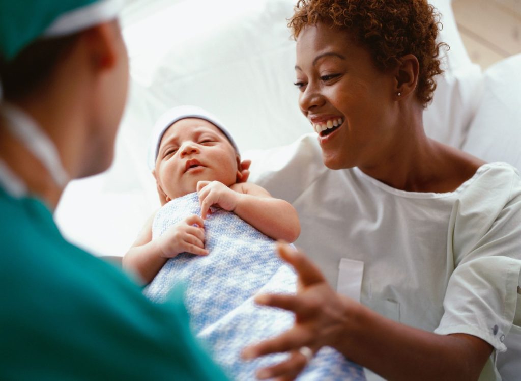 A woman holding a baby while another person looks on.