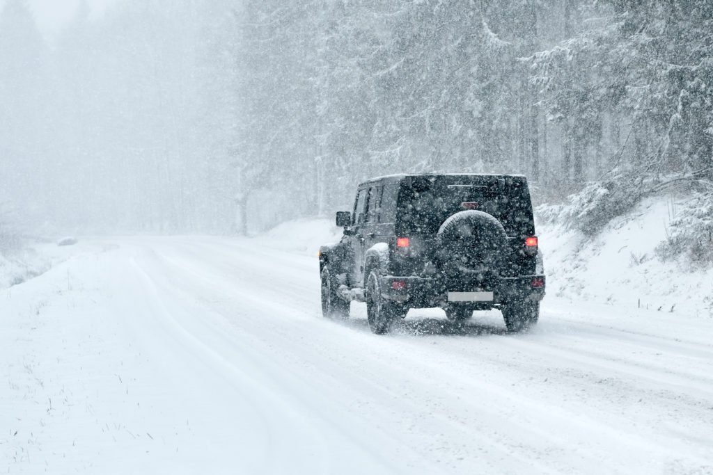 A jeep driving down the road in heavy snow.