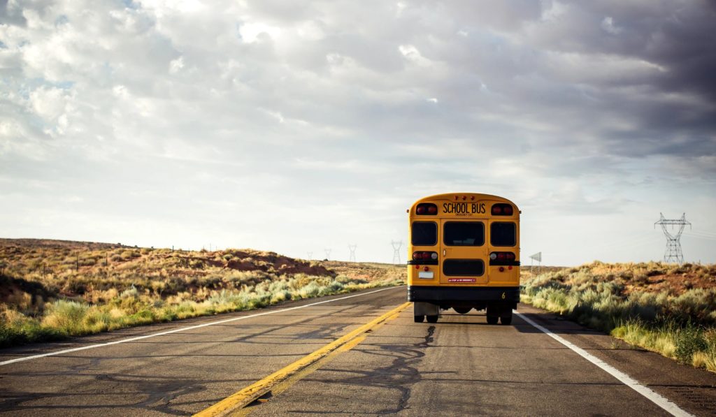 A school bus driving down the road under cloudy skies.