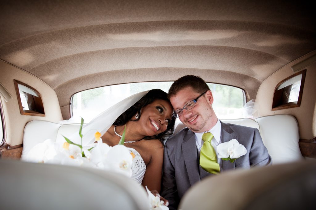 A bride and groom sitting in the back of a car.