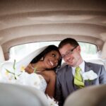 A bride and groom sitting in the back of a car.