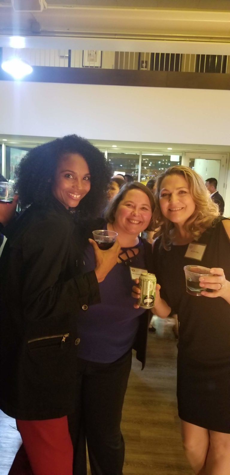 Three women are holding drinks at a party.