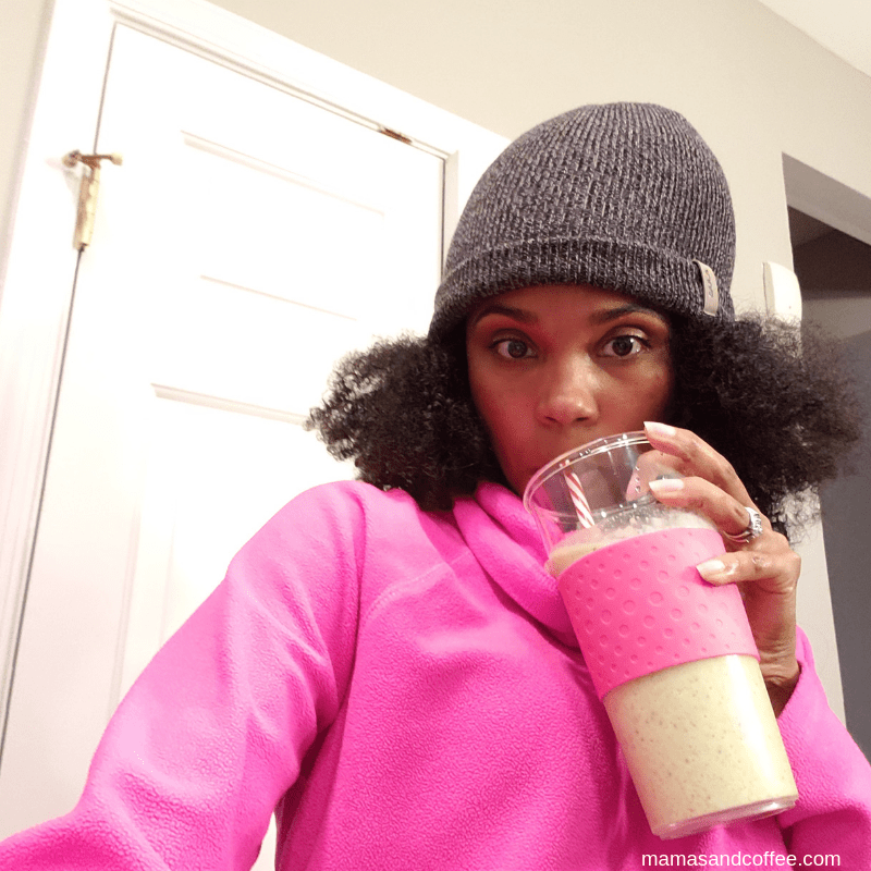 A woman in pink jacket drinking from cup.