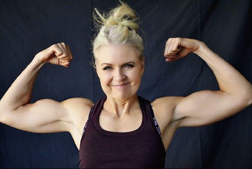 A woman showing off her muscles in front of a black background.