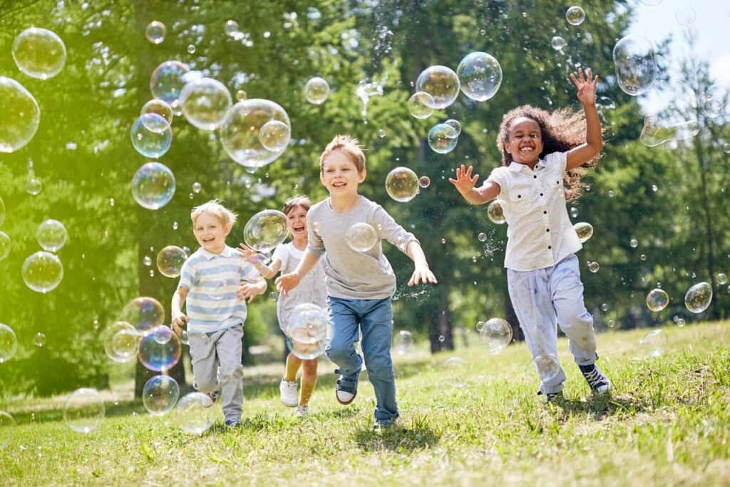 A group of children running through the grass with bubbles.