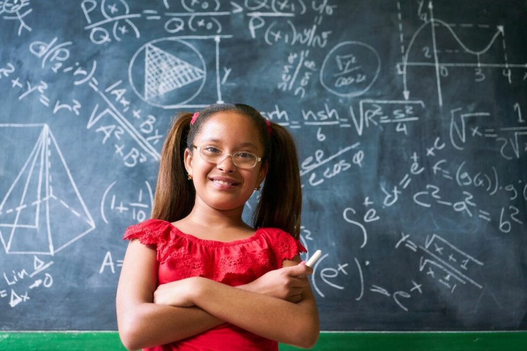 A girl in glasses standing next to a chalkboard.
