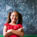 A girl in glasses standing next to a chalkboard.