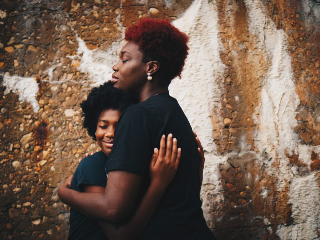 Two people hugging each other near a wall.