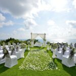 A wedding ceremony with white chairs and flowers.