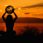 A person holding up the earth in front of an orange sky.