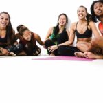 A group of women sitting on the ground in yoga poses.