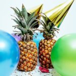 Two pineapples with party hats on them and balloons