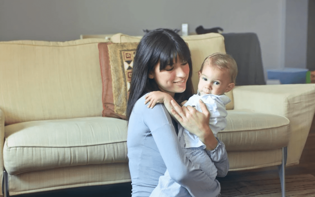 A woman holding a baby in front of a couch.